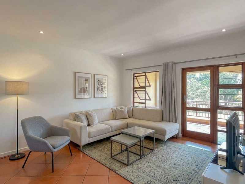A bright living room featuring terracotta floor tiles, recessed downlighting, and direct access to an outdoor balcony through a timber-framed glass door.