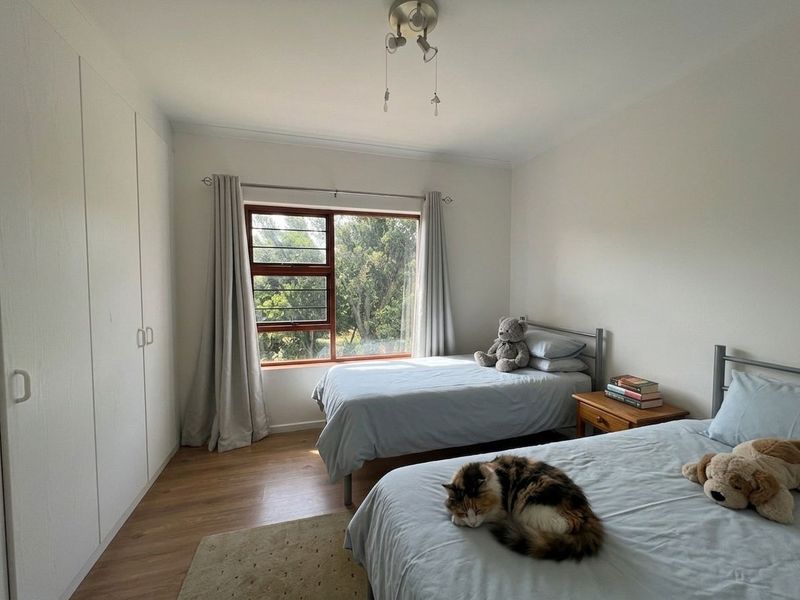 A well-lit bedroom featuring laminate flooring, built-in cupboards, and a large window with views of the surrounding greenery.