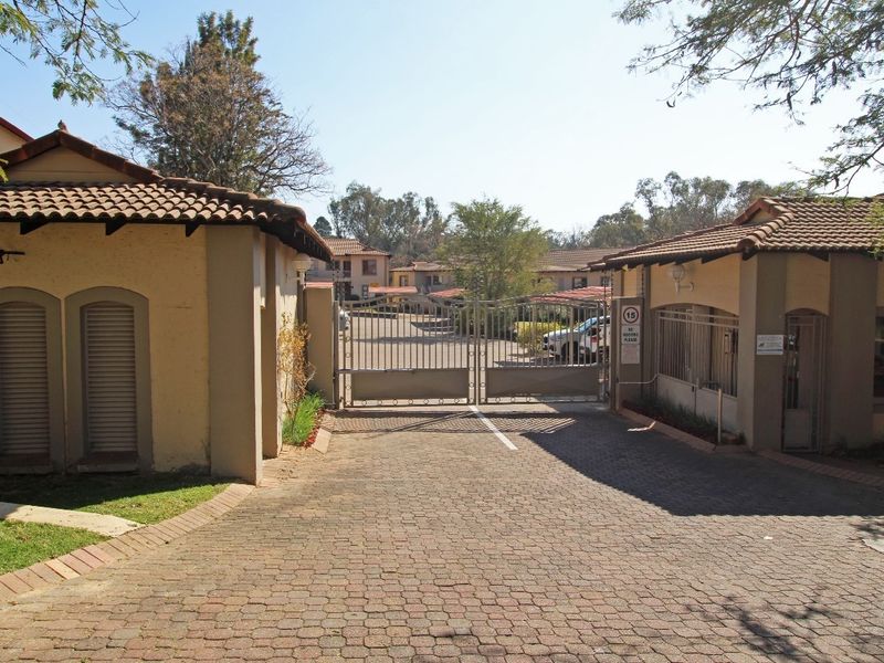A secure gated entrance to the apartment complex featuring a paved driveway and well-maintained perimeter structures with tiled roofing.