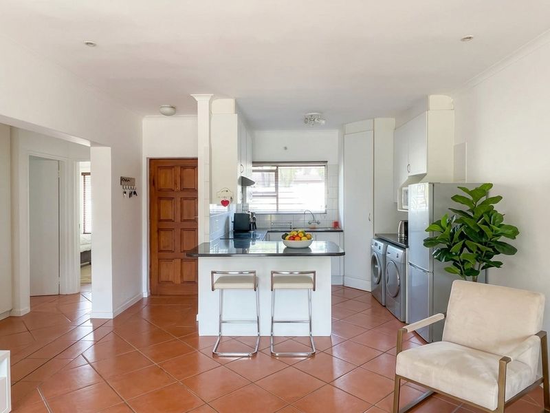 Open-plan kitchen featuring white cabinetry, granite countertops, and tiled flooring, seamlessly integrated with the living area and laundry space.