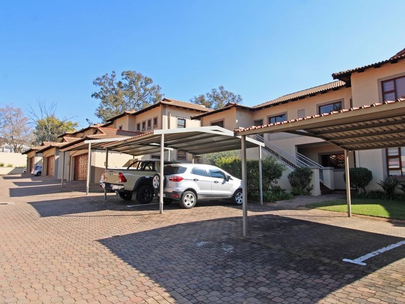 Exterior view of an apartment complex featuring covered parking bays, paved driveway, and multi-level residential units with tiled roofing.