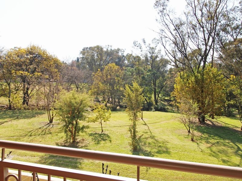 A scenic elevated view overlooking a lush green parkland with mature trees, captured from a private apartment balcony.