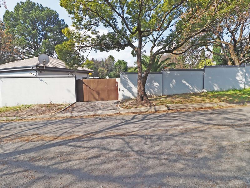 Street view of the property entrance featuring a perimeter wall, mature trees, and a metal driveway gate.