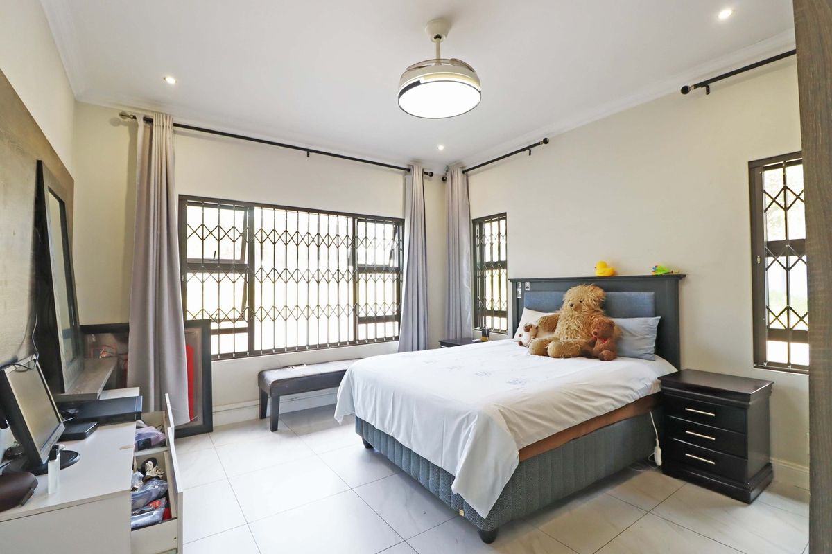 A well-lit bedroom featuring tiled flooring, a ceiling fan, and large windows fitted with security bars for added peace of mind.
