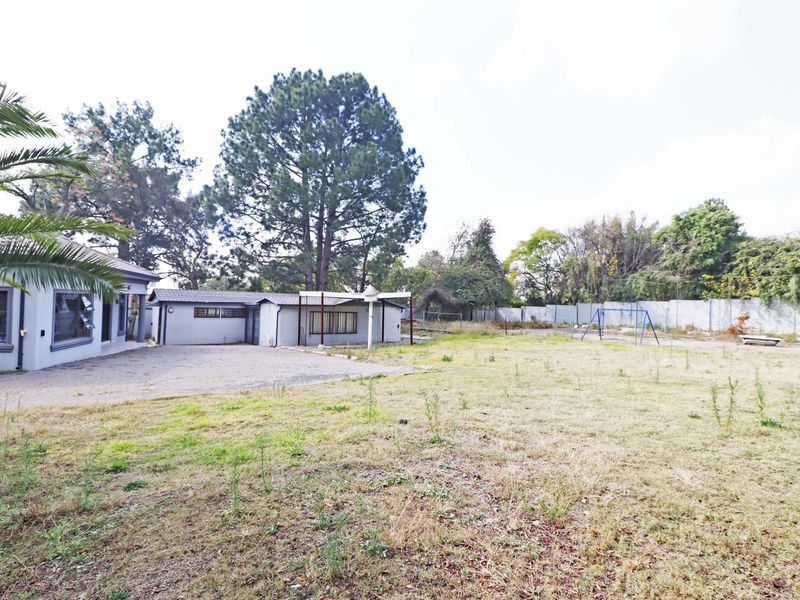 A spacious rear yard featuring a paved patio area, established trees, and perimeter walling, offering significant potential for landscaping and outdoor development.