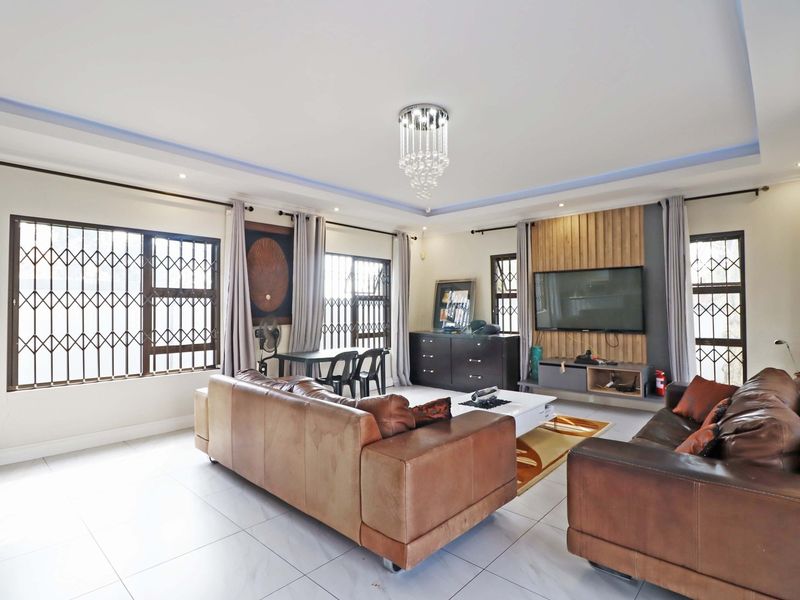 Spacious living room featuring tiled flooring, a timber slat feature wall, recessed ceiling lighting, and a decorative crystal chandelier.