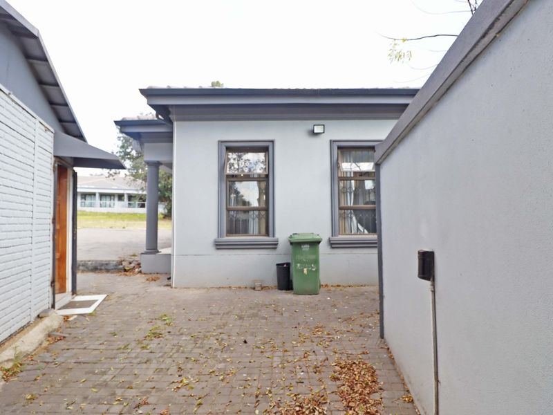 A paved rear courtyard area featuring exterior wall lighting and windows with security bars, providing a functional outdoor space.