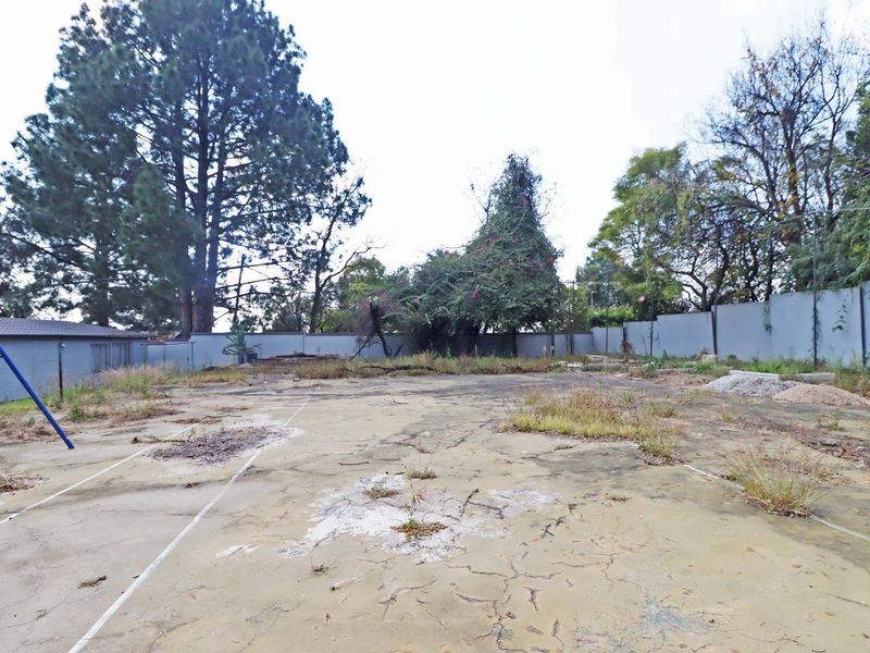 A vacant residential plot featuring a large cracked concrete slab, perimeter walling, and mature trees, offering a blank canvas for future development.
