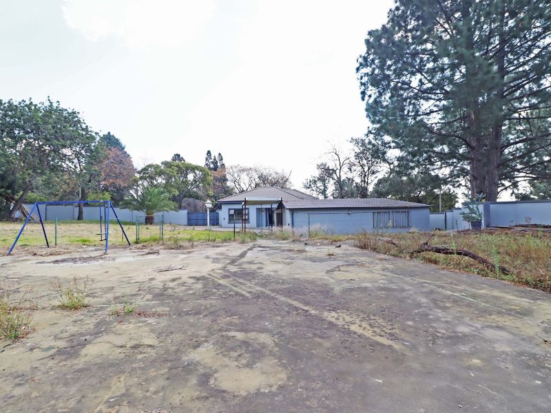 Rear view of the property featuring a large concrete paved area, perimeter walling, and established trees on a spacious residential lot.