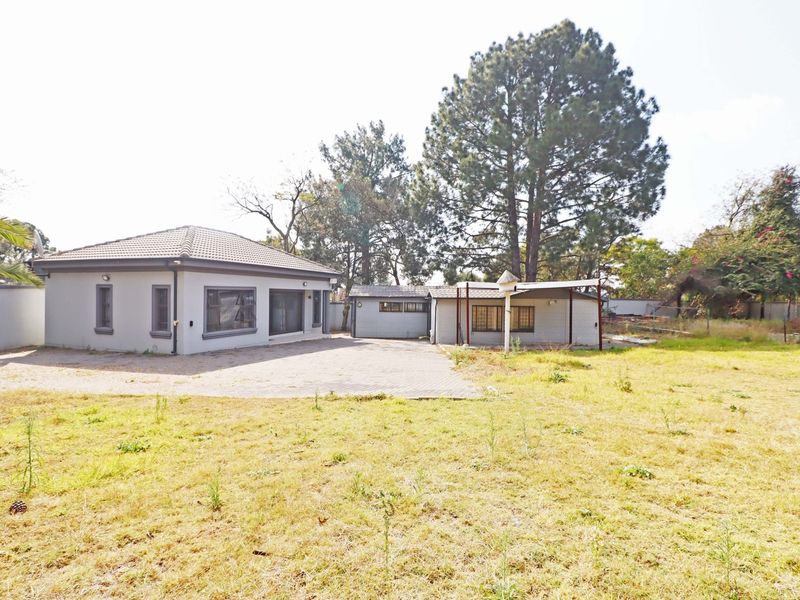 Rear view of the residential property featuring a paved area, covered patio, and established garden with mature trees.