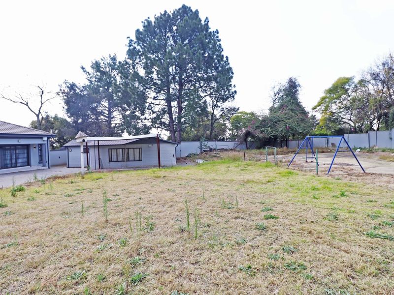 A spacious rear yard featuring a large lawn, paved sections, and an outbuilding, enclosed by a perimeter boundary wall.