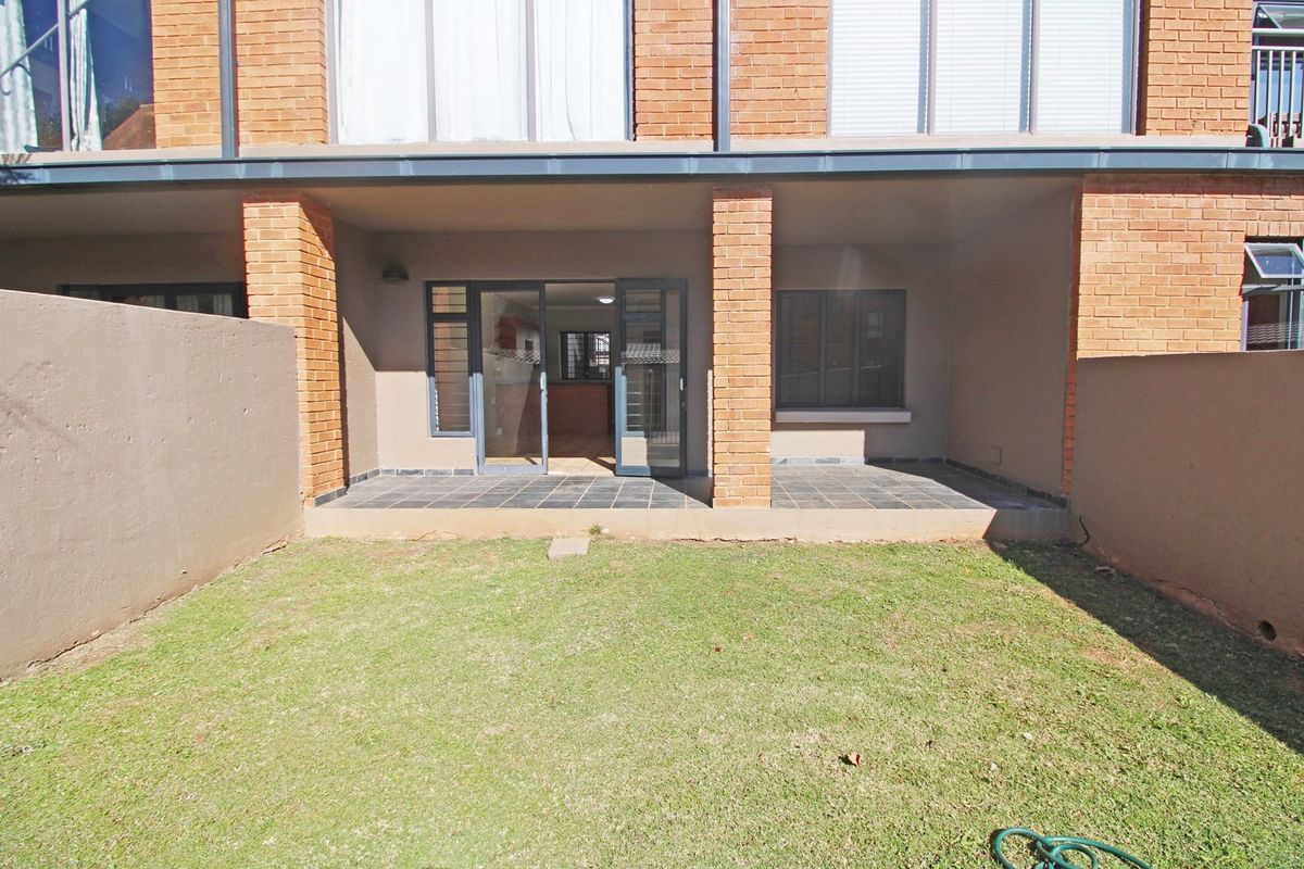 Rear view of the apartment featuring a private patio with tiled flooring, brick pillars, and a small garden area accessible via sliding glass doors.