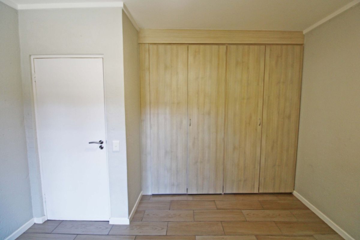 A clean, empty bedroom featuring neutral tiled flooring and ample built-in wooden cupboards, providing a versatile space ready for personalization.