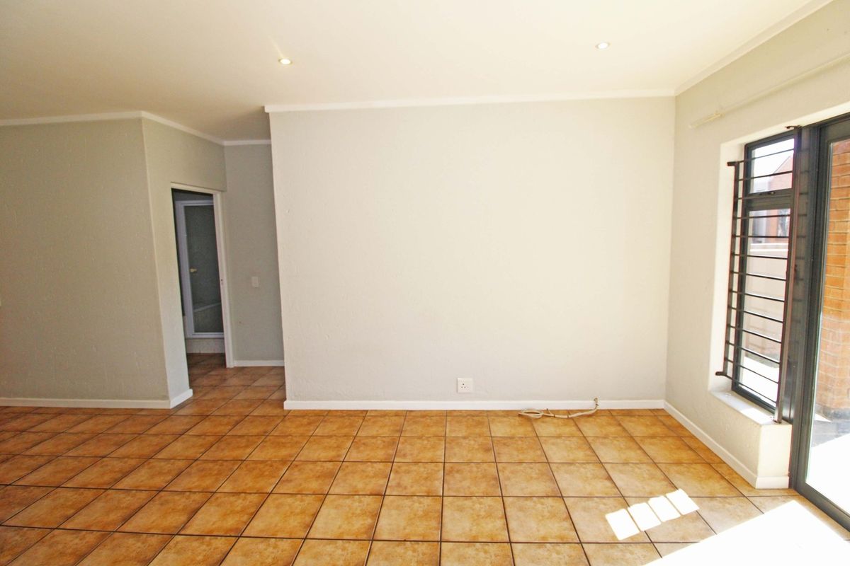 An empty living room featuring ceramic floor tiles, recessed downlighting, and a sliding door with security bars leading to an outdoor area.