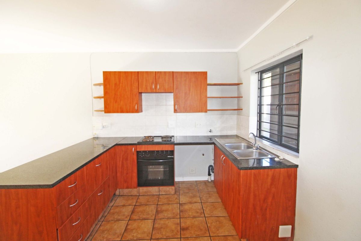 Functional kitchen featuring wood-finish cabinetry, granite countertops, built-in oven and hob, and a double basin sink with tiled flooring.