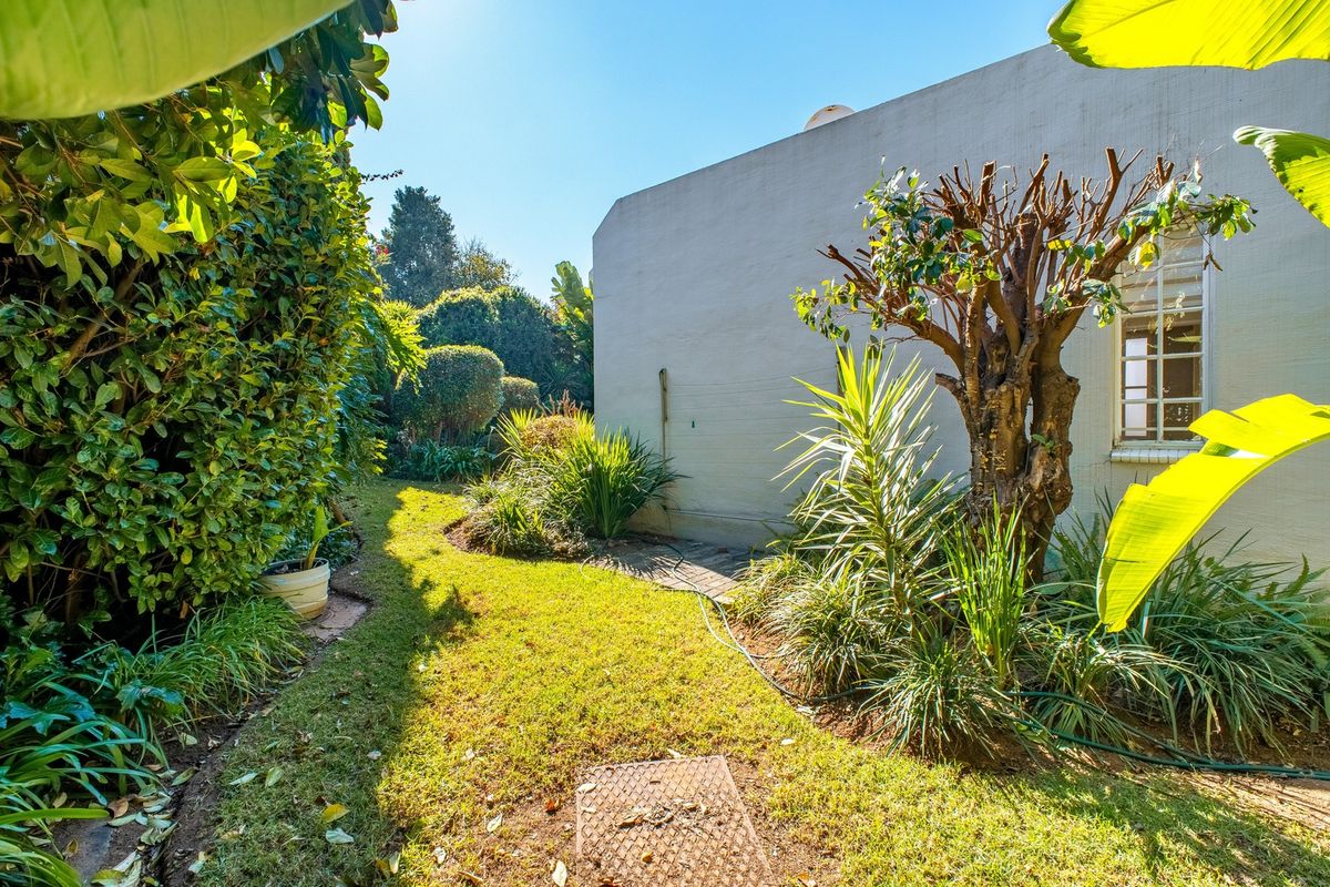 A private rear garden area featuring a well-maintained lawn, established greenery, and a side wall of the townhouse with a window.