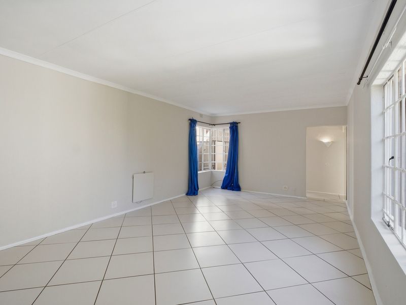 A bright, spacious, and empty living room featuring neutral tiled flooring, a corner window, and a wall-mounted heater.