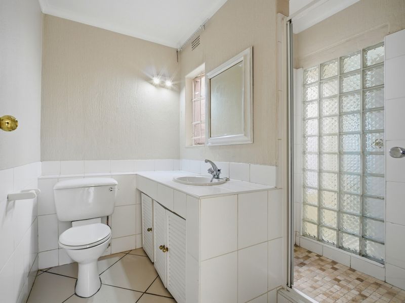 A functional bathroom featuring a vanity with a drop-in sink, a toilet, and a shower enclosure with a distinctive glass block wall.