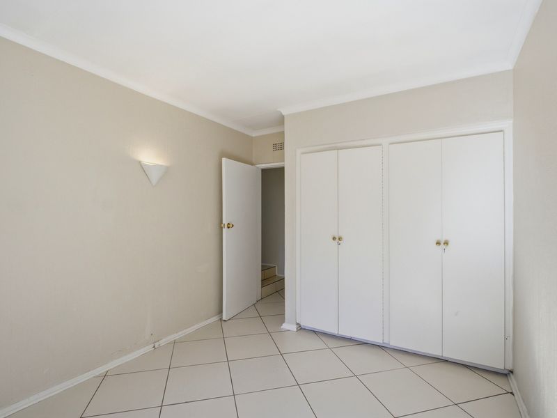 An empty bedroom featuring neutral tiled flooring, built-in cupboards, and a wall-mounted light fixture, offering a clean and versatile space.