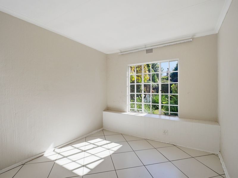 A bright, empty bedroom featuring neutral tiled flooring, a large grid-pattern window with a tiled ledge, and clean, light-toned walls.