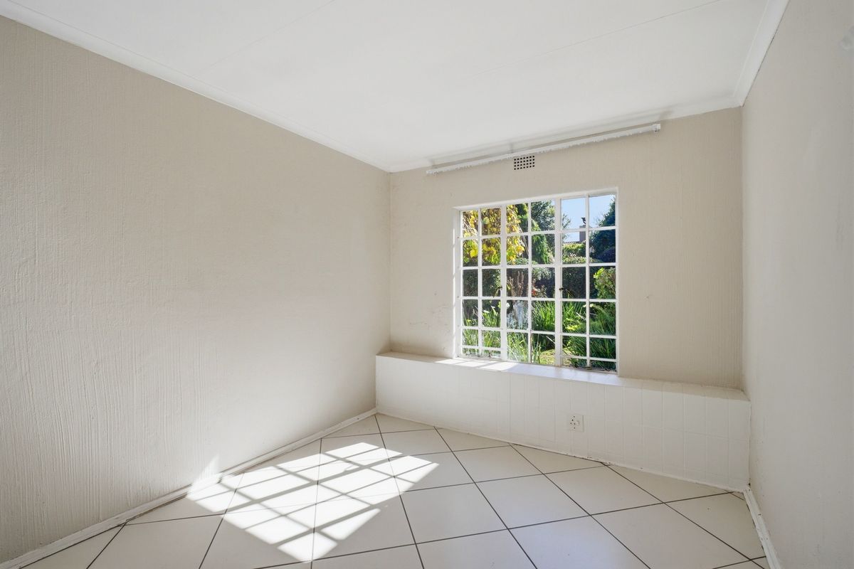 A bright, empty bedroom featuring neutral tiled flooring, a large grid-pattern window with a tiled ledge, and clean, light-toned walls.