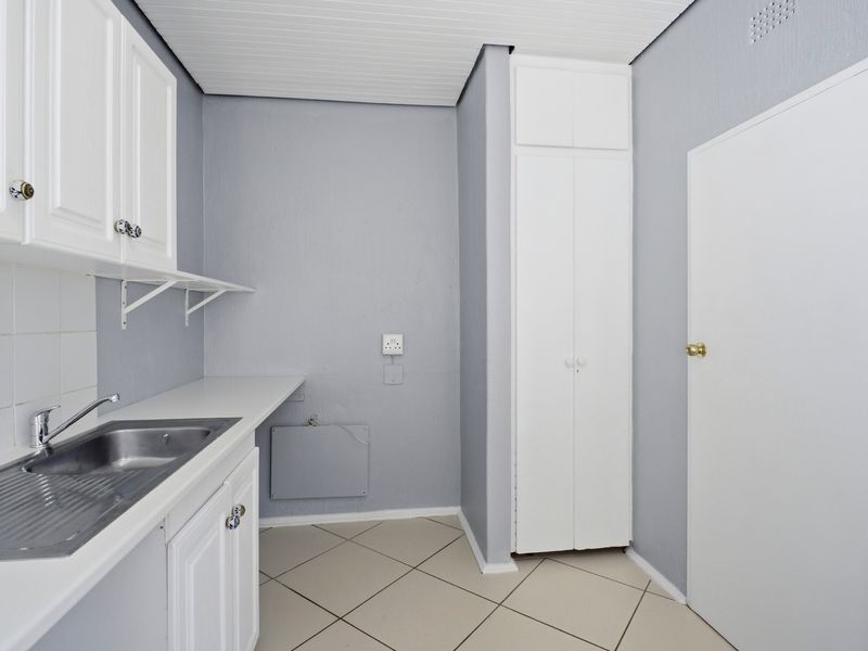 A functional laundry room featuring built-in cabinetry, a stainless steel sink, and tiled flooring with ample storage space.