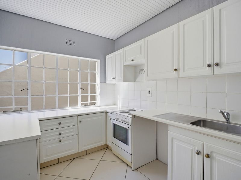 A functional kitchen featuring white cabinetry, tiled backsplash, laminate countertops, and a freestanding electric stove, illuminated by a large grid-pattern window.