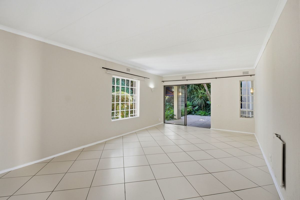 A bright, spacious, and empty living room featuring neutral tiled flooring, large grid-pattern windows, and a sliding glass door leading to a patio.