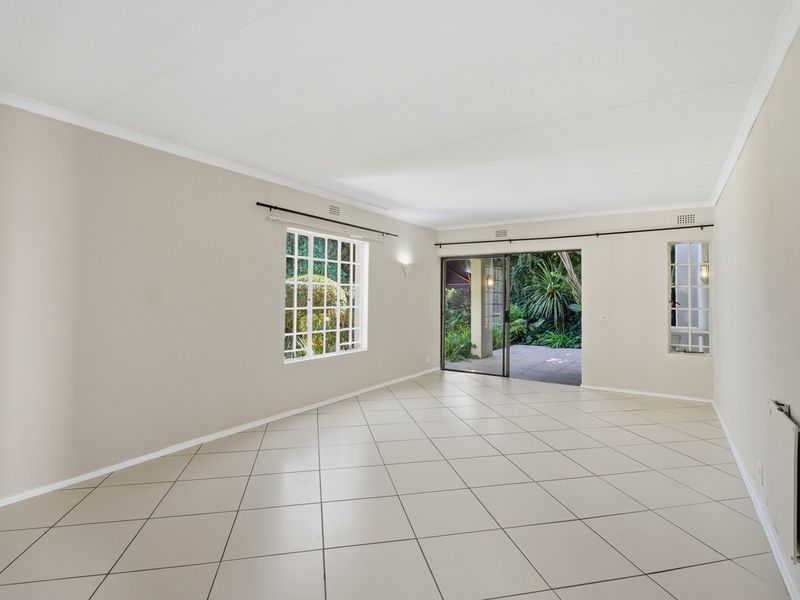 A bright, spacious, and empty living room featuring neutral tiled flooring, large grid-pattern windows, and a sliding glass door leading to a patio.