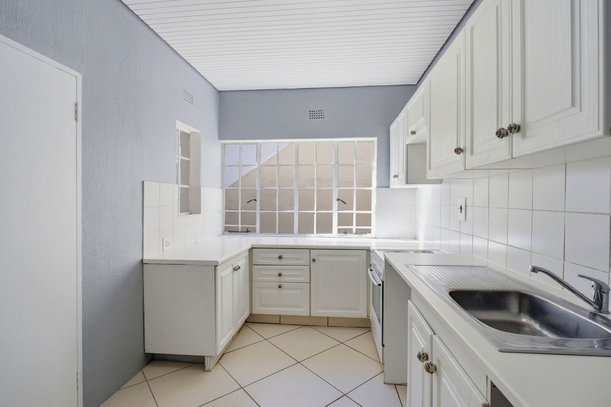A functional kitchen featuring white cabinetry, tiled splashbacks, a stainless steel sink, and tiled flooring, offering a clean and neutral space for culinary activities.