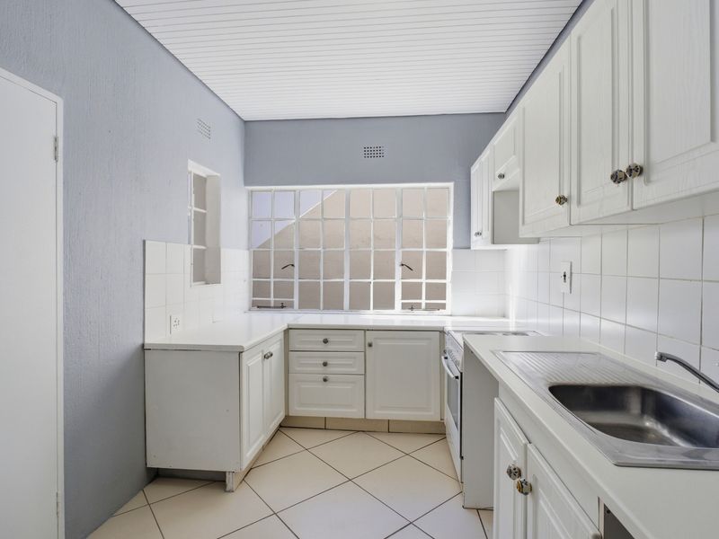 A functional kitchen featuring white cabinetry, tiled splashbacks, a stainless steel sink, and tiled flooring, offering a clean and neutral space for culinary activities.