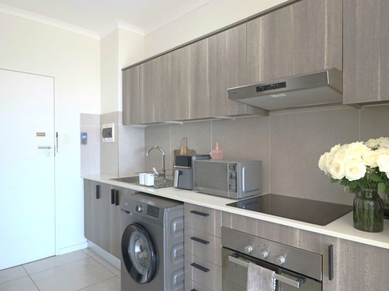 Modern kitchen featuring sleek wood-grain cabinetry, integrated stainless steel appliances, a tiled backsplash, and a functional layout with a built-in oven and hob.
