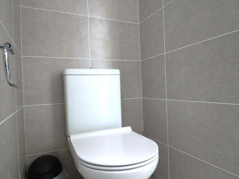 A clean, modern bathroom featuring neutral grey wall tiles and a white toilet suite.
