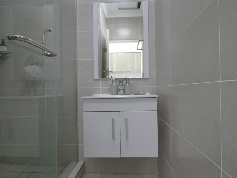 Modern bathroom featuring a wall-mounted vanity, glass shower enclosure, and neutral ceramic wall tiling.