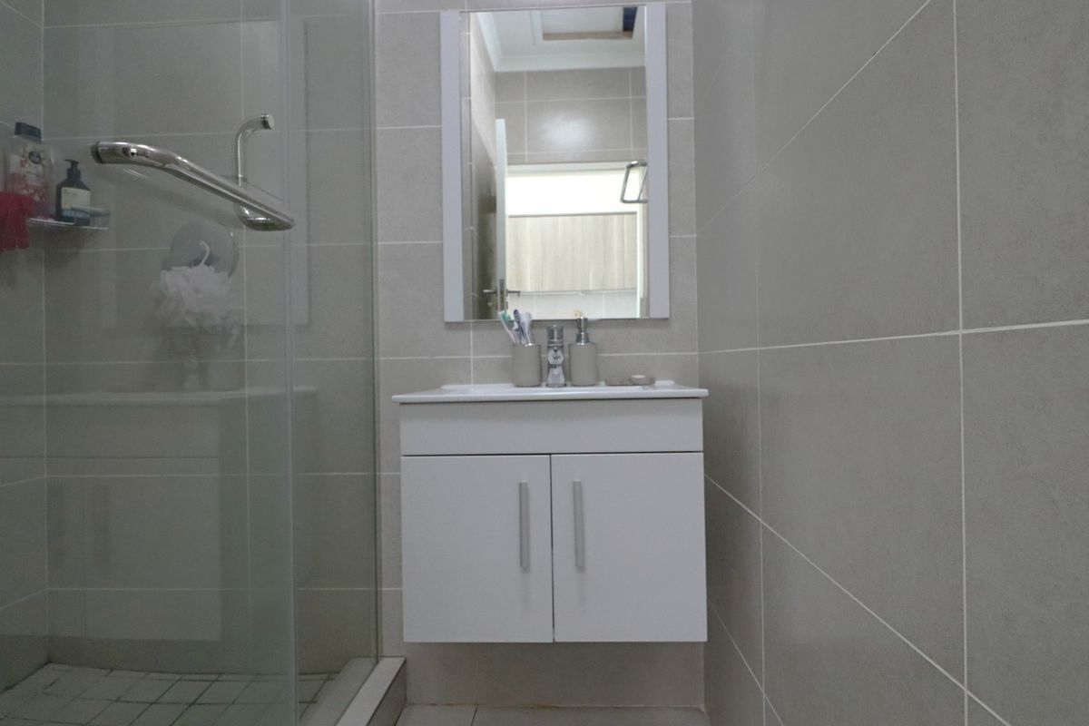 Modern bathroom featuring a wall-mounted vanity, glass shower enclosure, and neutral ceramic wall tiling.