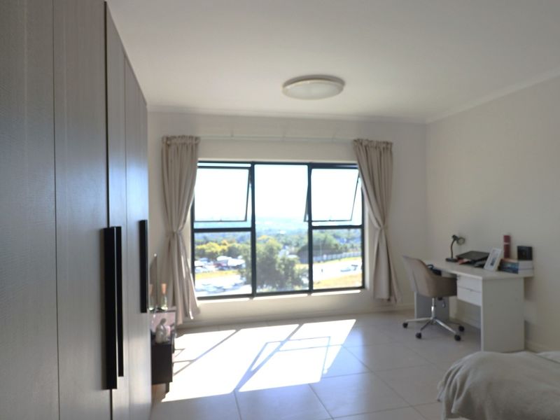 A bright bedroom featuring built-in cupboards, tiled flooring, and large aluminium windows offering natural light and scenic views.
