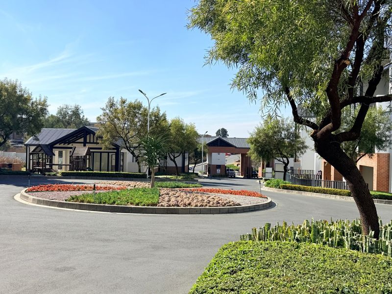 A well-maintained apartment complex entrance featuring a landscaped roundabout, paved driveway, and secure gatehouse access.
