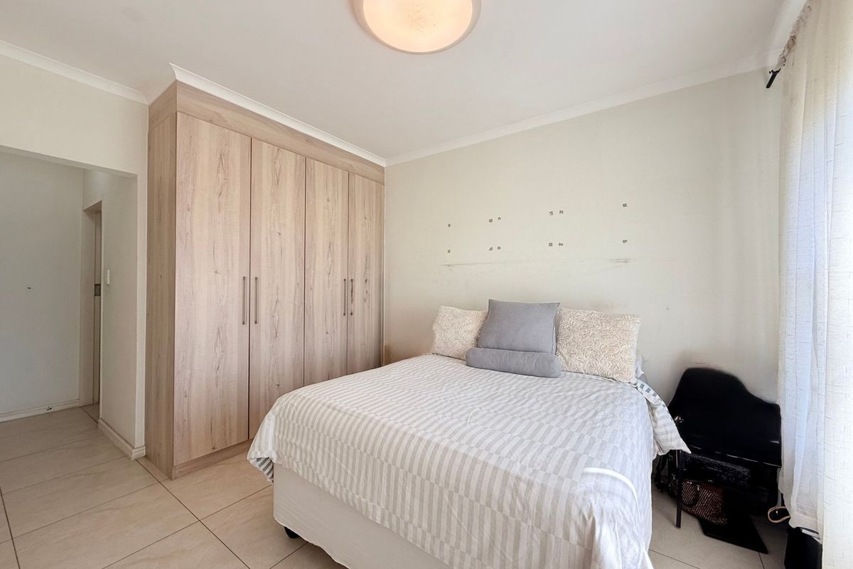 A bedroom featuring light wood-finish built-in cupboards, tiled flooring, and a central ceiling light fixture.