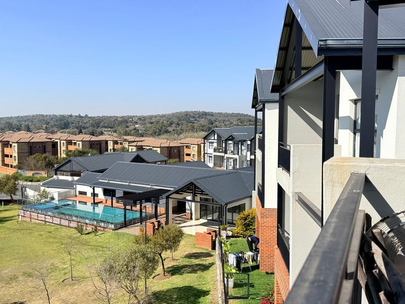 Elevated view of the apartment complex grounds, featuring a communal swimming pool, landscaped gardens, and modern architectural building exteriors.