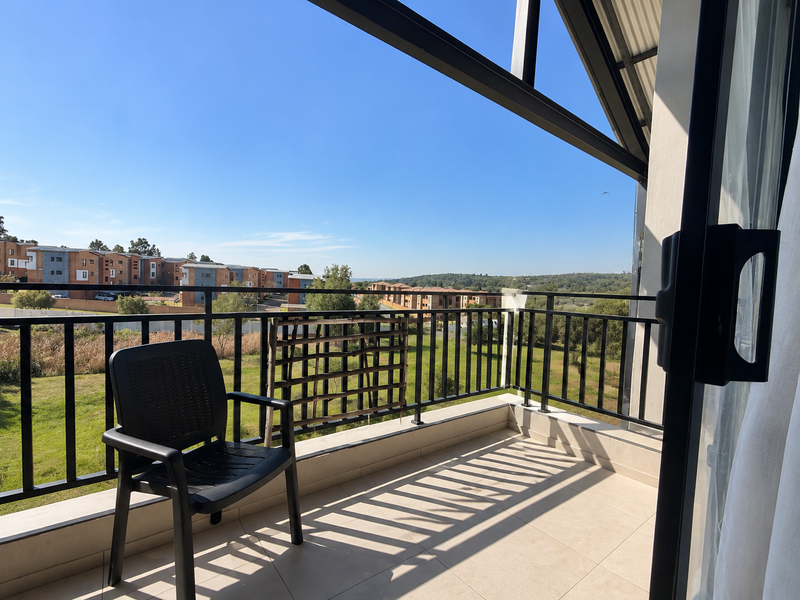 A spacious balcony featuring tiled flooring and a metal balustrade, offering expansive views of the surrounding residential estate and landscape.