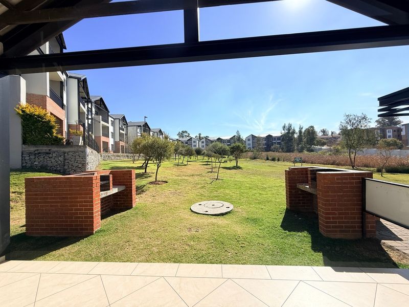 A communal outdoor area featuring brick braai facilities, a tiled patio, and a well-maintained lawn within an apartment complex.