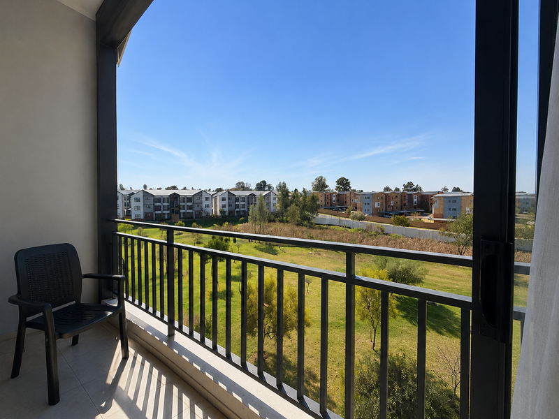 A covered balcony featuring tiled flooring and a metal balustrade, offering an open view of the surrounding apartment complex and green space.