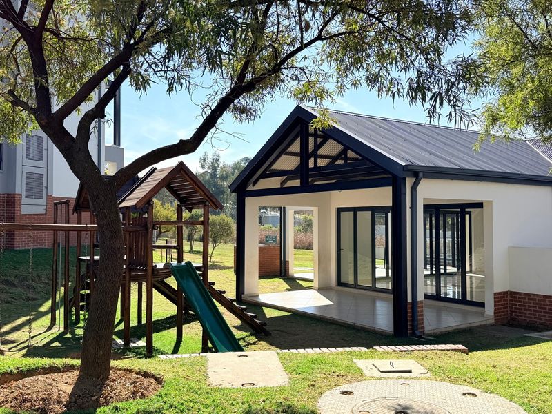 A well-maintained communal outdoor area featuring a covered patio with tiled flooring, modern aluminum sliding doors, and an adjacent children's playground.