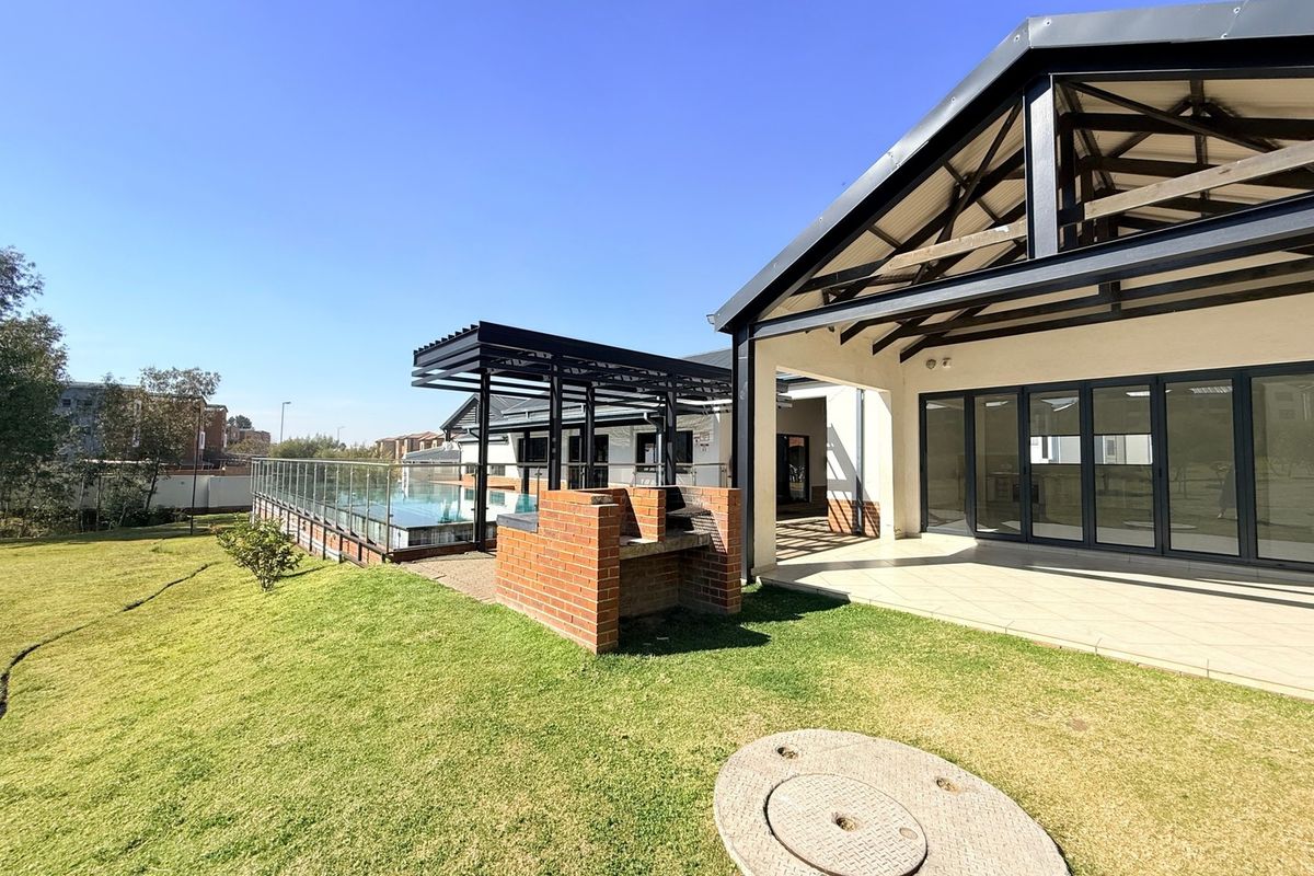 Rear exterior view featuring a covered patio with folding glass doors, a built-in brick braai, and a landscaped garden area.