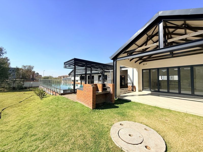 Rear exterior view featuring a covered patio with folding glass doors, a built-in brick braai, and a landscaped garden area.