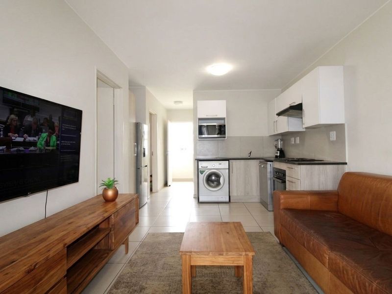 An open-plan living area featuring a compact kitchen with built-in cabinetry, integrated appliances, and tiled flooring throughout the space.