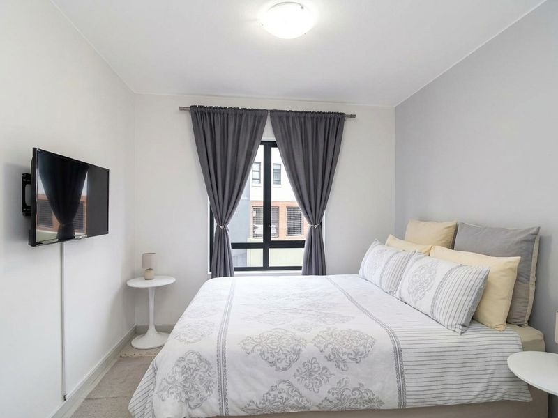 A well-maintained bedroom featuring neutral walls, a large window for natural light, and a wall-mounted television setup.