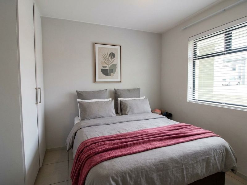 A well-maintained bedroom featuring neutral walls, tiled flooring, a built-in wardrobe, and venetian blinds for privacy.