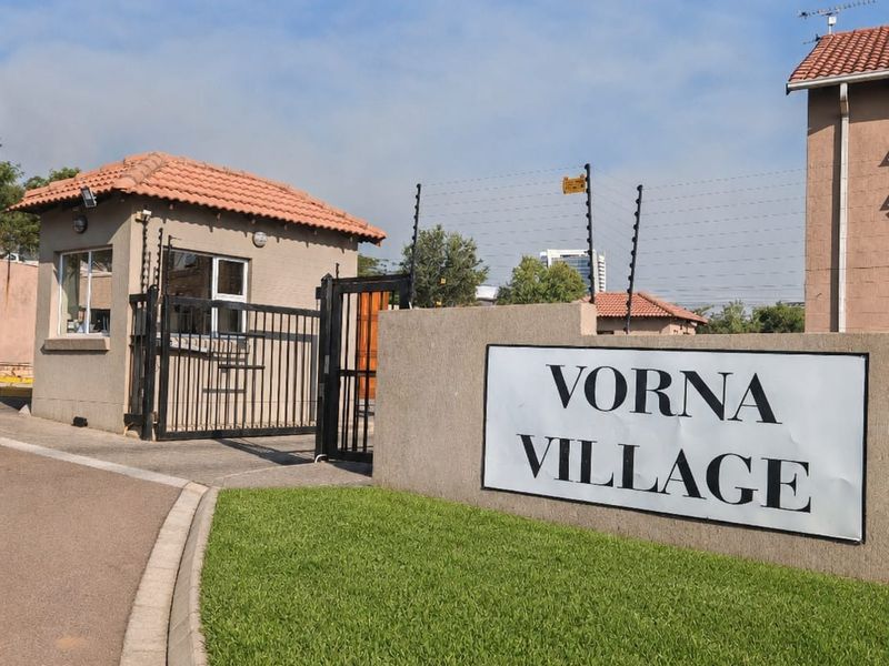 The entrance to Vorna Village featuring a security guard house, electric fencing, and a paved driveway leading into the complex.