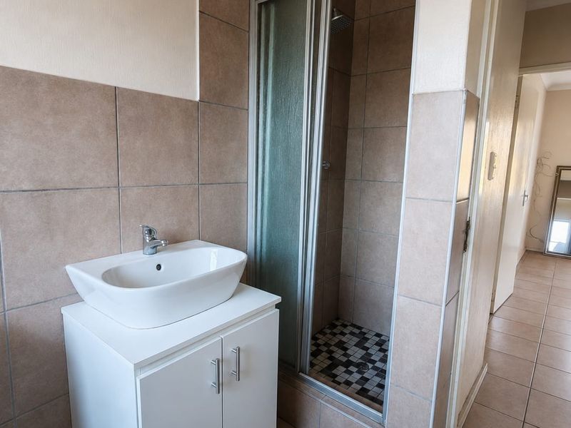 A functional bathroom featuring a white vanity cabinet with a vessel sink, a tiled shower enclosure, and neutral wall and floor tiling.